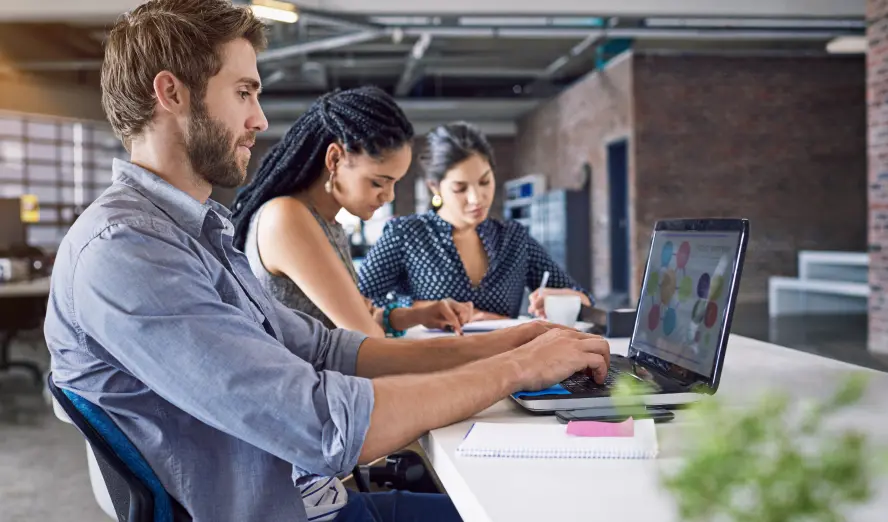 Three people collaborating on a laptop in a professional office setting.